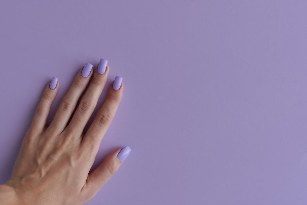 Female's hand with nails of purple color. Gelish manicure. Square fingernails with permanent nail polish of trendy lavender color